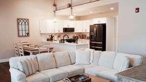 A modern kitchen with white cabinets, a stainless steel refrigerator, and a dining area with a white table and chairs. - Spacious 2BR Condo - Minutes to DT Mystic (Stonington)