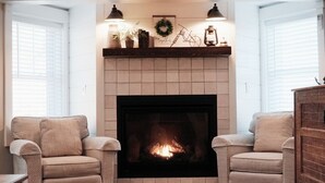 A cozy living room with a fireplace, two armchairs, and a mantelpiece with decorative items. - Spacious 2BR Condo - Minutes to DT Mystic (Stonington)