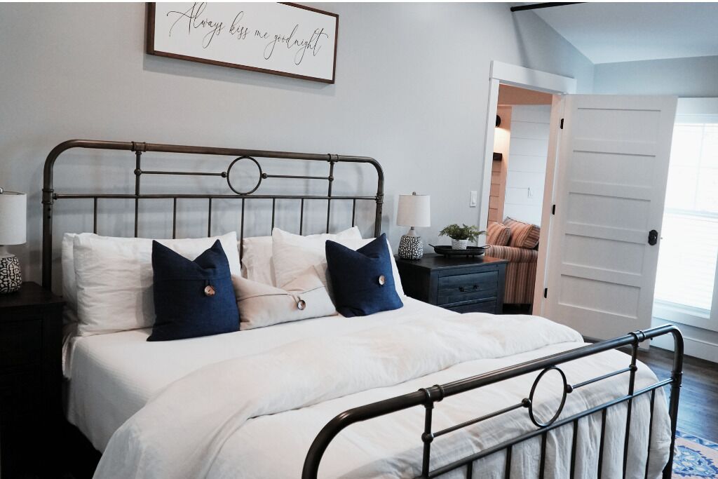 Un lit bien fait, avec des oreillers blancs et bleus, une tête de lit en métal et une table de chevet avec une lampe.