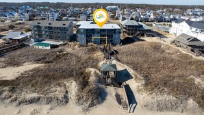 An aerial view of a coastal residential area with multiple houses, a prominent blue building with balconies, and a sandy beach area. - Ocean's Outside: Relaxing Oceanfront Escape (Kill Devil Hills)