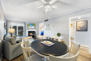 A modern living room with a fireplace, a dining table, and a sofa. - Ocean's Outside: Relaxing Oceanfront Escape (Kill Devil Hills)