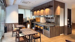 A modern kitchen with a central island, bar stools, and a dining area with wooden tables and chairs. - TORANOMONHOLIC HOTEL (Tokyo)