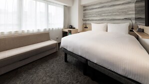 A modern hotel room with a large bed, a sofa, a desk, and a wall-mounted TV. - TORANOMONHOLIC HOTEL (Tokyo)
