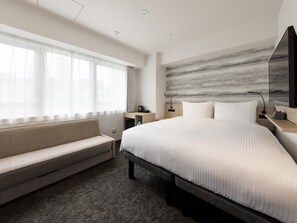 Ein modernes Hotelzimmer mit einem großen Bett, einer Couch, einem Schreibtisch und einem an der Wand montierten Fernseher.