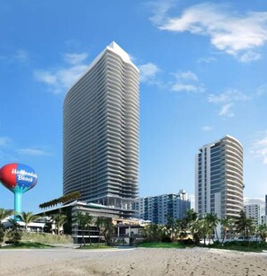 A modern hotel with a curved facade, located near a beach with palm trees and a sign for 'Hampton Beach'. - 2bedroom Lyfe resort Apartment over the beach (Hollywood)