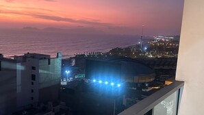 A balcony with a view of the city at dusk, featuring buildings and a distant shoreline. - Cozy apartment with ocean view (Lima)