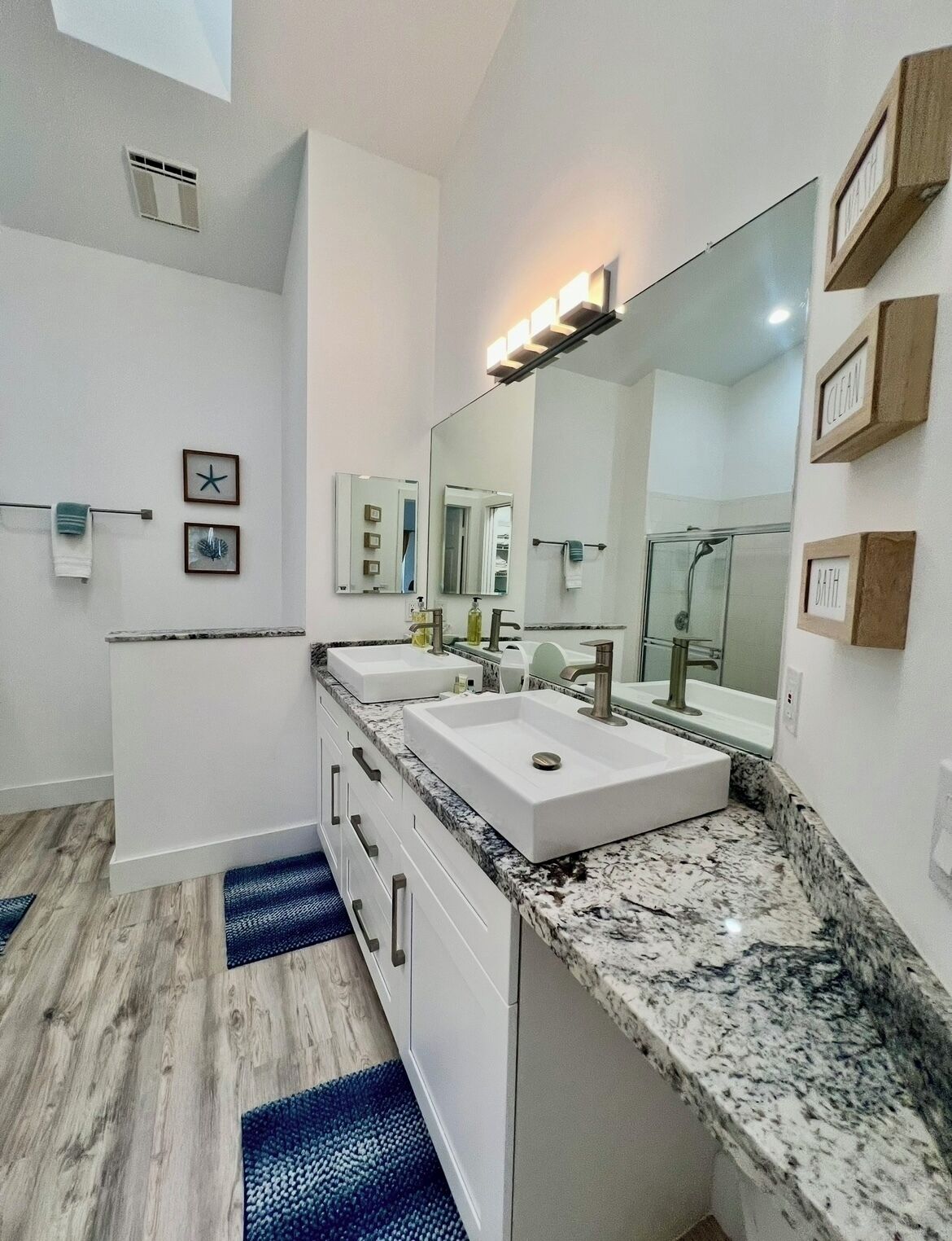 A modern bathroom with a large mirror, two sinks, and a shower.