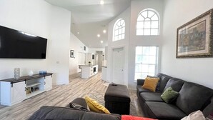 A spacious living room with a large flat-screen TV, a dark-colored sofa with cushions, a wooden coffee table, and a red throw blanket. - Serene 2-bedroom villa near beach in lovely Boca Raton (Boca Raton)