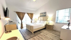A hotel room with a bed, bedside tables, a desk, a mirror, a ceiling fan, and a window. - Serene 2-bedroom villa near beach in lovely Boca Raton (Boca Raton)