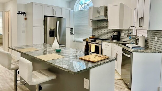 A modern kitchen with white cabinetry, a large island with a marble countertop, and a built-in oven. - Serene 2-bedroom villa near beach in lovely Boca Raton (Boca Raton)