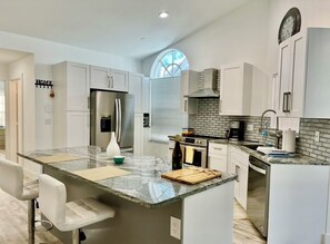 A modern kitchen with white cabinetry, a large island with a marble countertop, and a built-in oven. - Serene 2-bedroom villa near beach in lovely Boca Raton (Boca Raton)