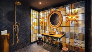 Ein Badezimmer mit einem großen Spiegel, einem goldfarbenen Waschbecken und einer Dusche mit goldfarbener Duschbrause.