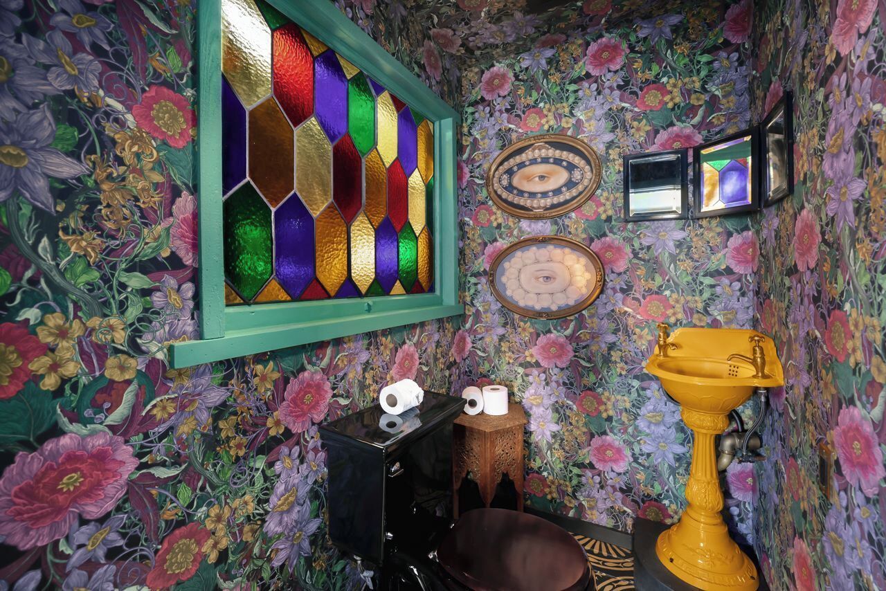 Una stanza con carta da parati floreale, una finestra a vetri colorati e un lavabo su piedistallo giallo.