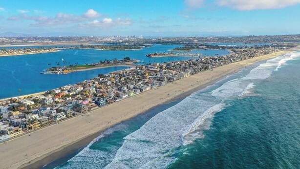 Een kuststadsgezicht met een lang strand, helderblauw water en een dichtbebouwd stedelijk gebied.