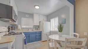 Een moderne keuken met blauwe kastjes, een witte eettafel en een potplant.