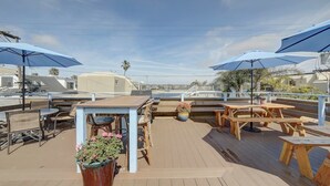 Een terras buiten met houten tafels en stoelen, parasols en potplanten.