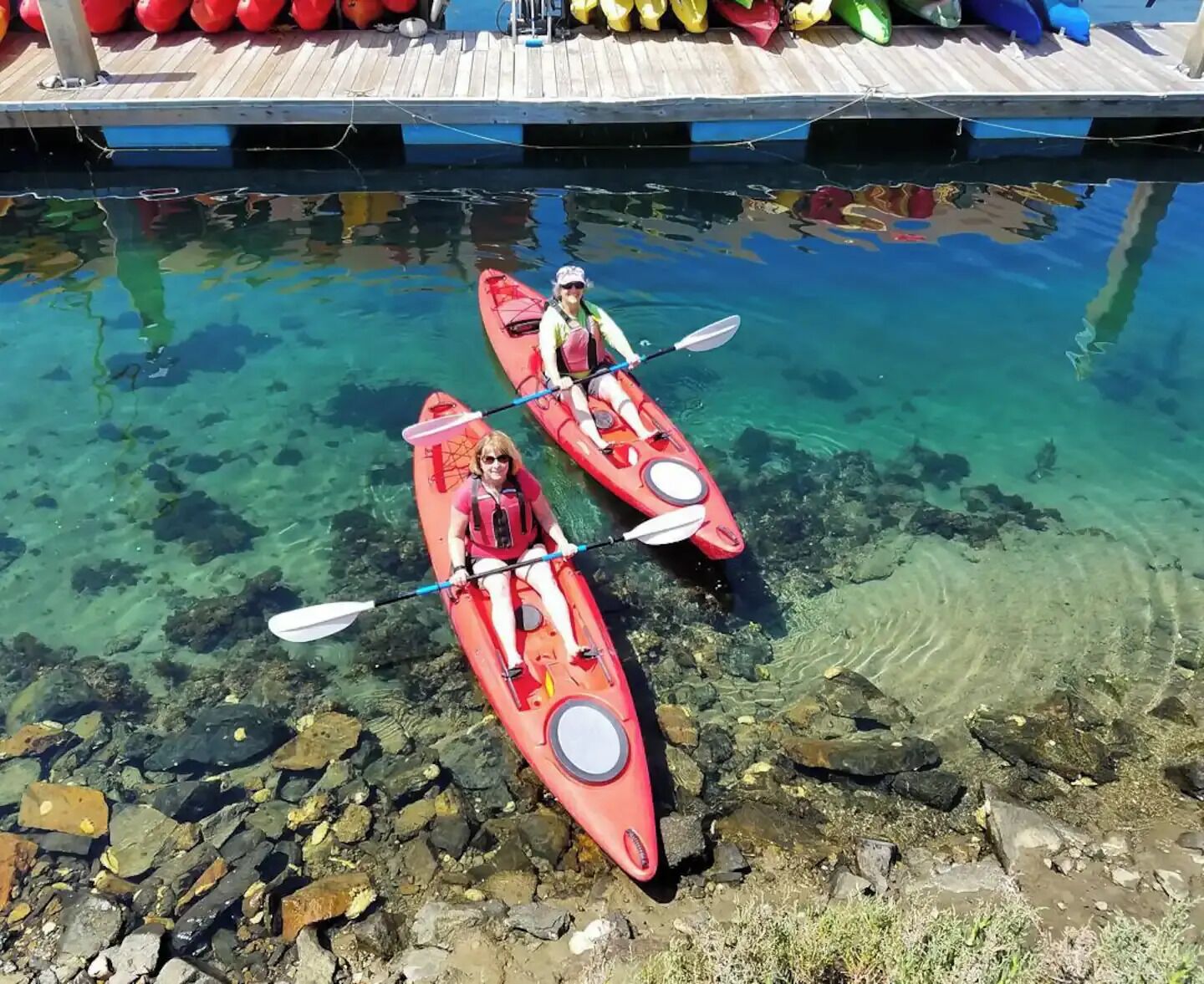 Two kayaks on a clear water body with a wooden dock in the background.