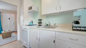 A modern kitchen with white cabinets, a stove, a microwave, and a sink. - Studio by the Beach • A/C, FREE Bikes & Beach Gear (San Diego)