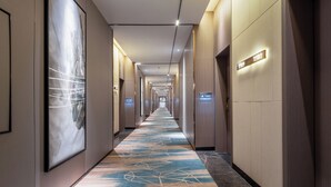 Un long couloir bien éclairé, avec des portes numérotées, une moquette à motifs et de grandes œuvres d’art abstrait accrochées aux murs.