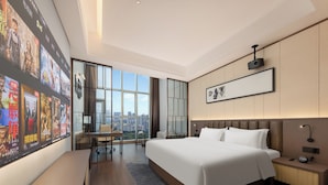 Une chambre d’hôtel moderne dotée d’un grand lit, d’un bureau et offrant une vue sur la ville grâce à de grandes fenêtres du sol au plafond.