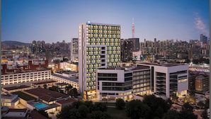Un grand hôtel à plusieurs étages, entouré d’autres immeubles et avec une vue sur le paysage urbain en arrière-plan.