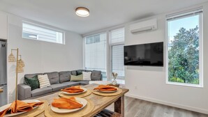 Ein modernes Wohnzimmer mit einer Couch, einem Esstisch mit Unterlagen und einem an der Wand befestigten Fernseher.