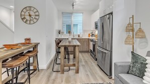 Eine moderne Küche mit einem Holztisch, Barhocker, einem Edelstahlkühlschrank und einer Uhr an der Wand.