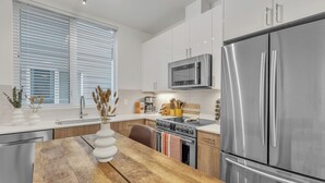 Eine moderne Küche mit weißen Schränken, Edelstahlgeräten und einem Holztisch.