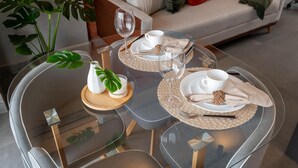 A dining table with a glass top, two white cups, wine glasses, and a napkin with a decorative knot. - Modern studio apartment with queen-size bed in Cityplex Osasco. (Osasco)