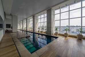 Une piscine intérieure moderne, dotée de grandes fenêtres et agrémentée de plantes en pot.