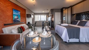 A modern hotel room with a bed, a sofa, a dining table with glasses, and a city view. - Modern studio apartment with queen-size bed in Cityplex Osasco. (Osasco)