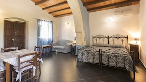 Ein Schlafzimmer mit Bett, Stuhl, Tisch und einem rundbogigen Durchgang.