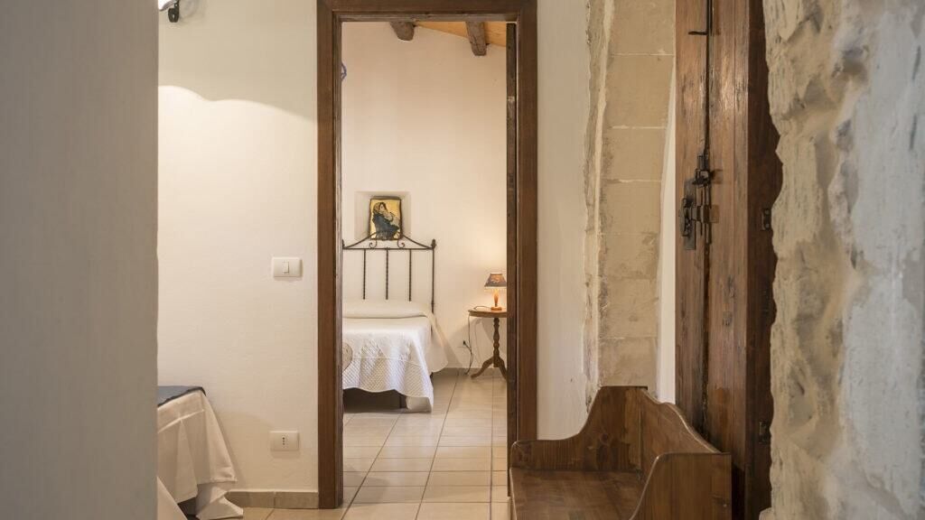 Un couloir étroit mène à une chambre à coucher qui contient un lit, une table de chevet et une lampe.