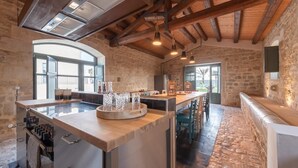 Une cuisine spacieuse dotée d’un grand îlot central, de murs en pierre et d’un plafond haut avec des poutres apparentes.