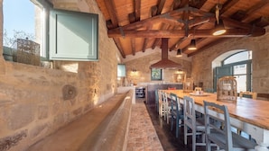 Un intérieur rustique en pierre, avec un long banc, des tables et des chaises en bois.