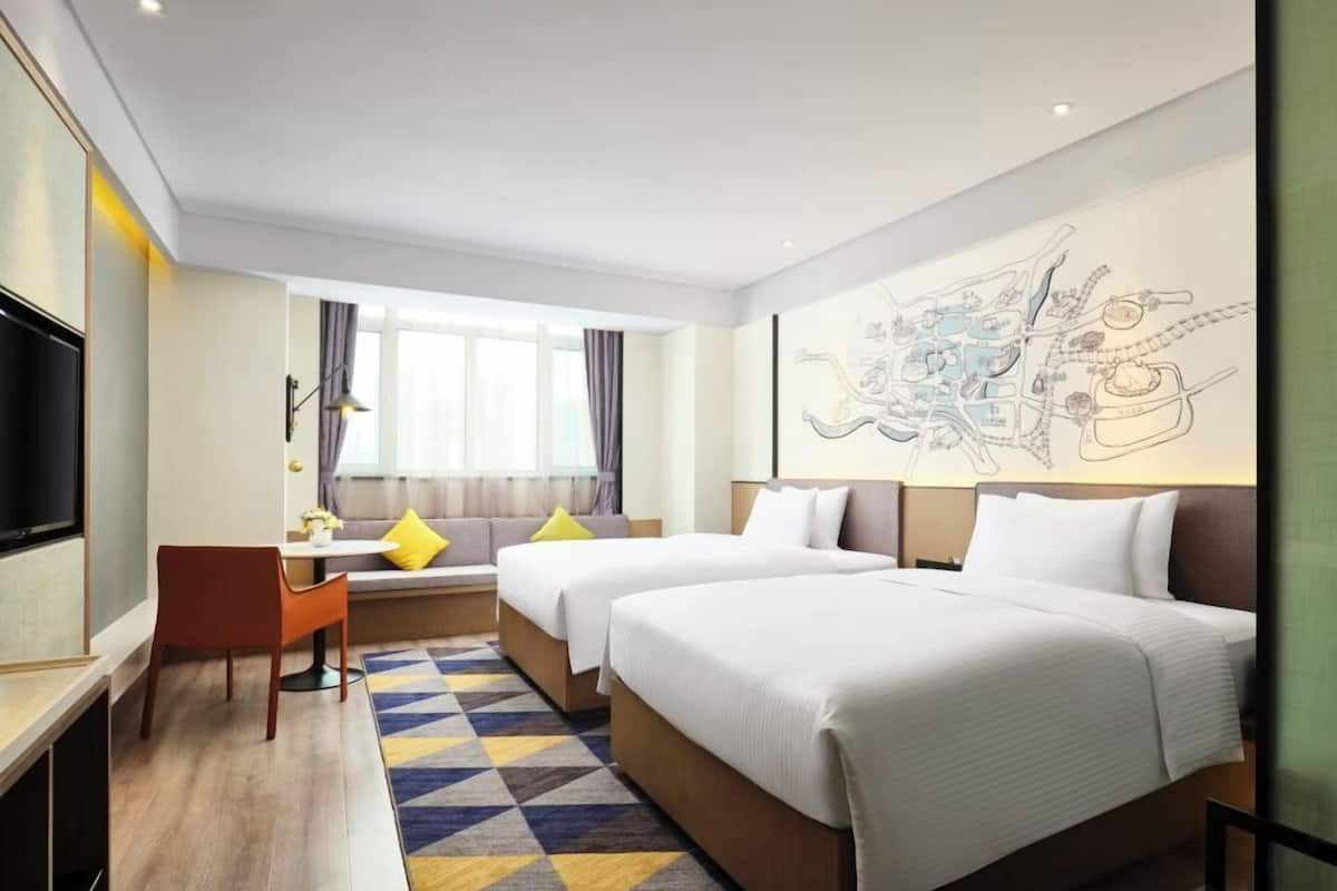 A hotel room with two beds, a desk, a chair, and a large window.