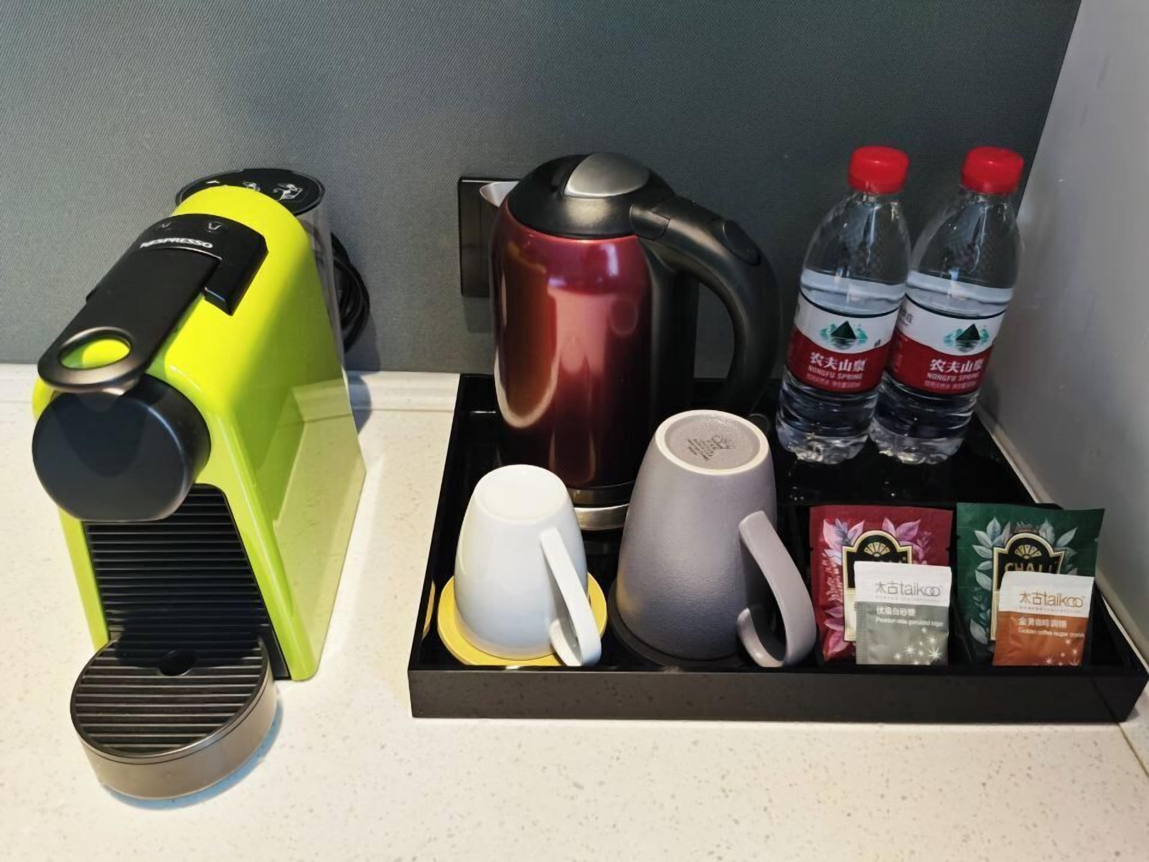 A coffee maker, a kettle, two bottles of water, a mug, a cup, and two tea bags on a tray.