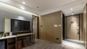 A modern hotel room with a large flat-screen TV, a desk with a computer, a small refrigerator, and a white bathtub. - Wanda Moments Heze (Heze)