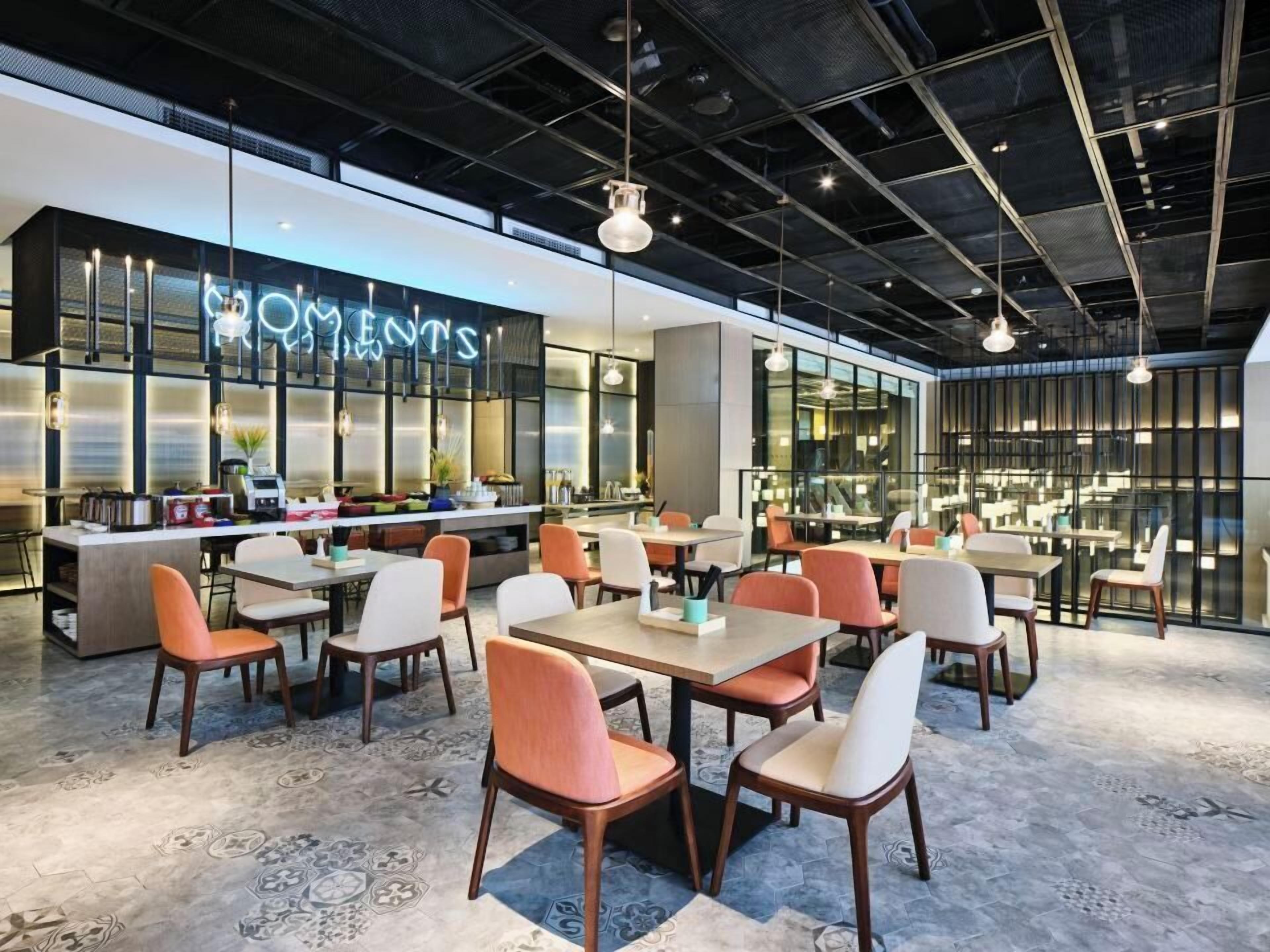 Un restaurante moderno con área de bar, varias mesas y sillas, y un letrero de neón.