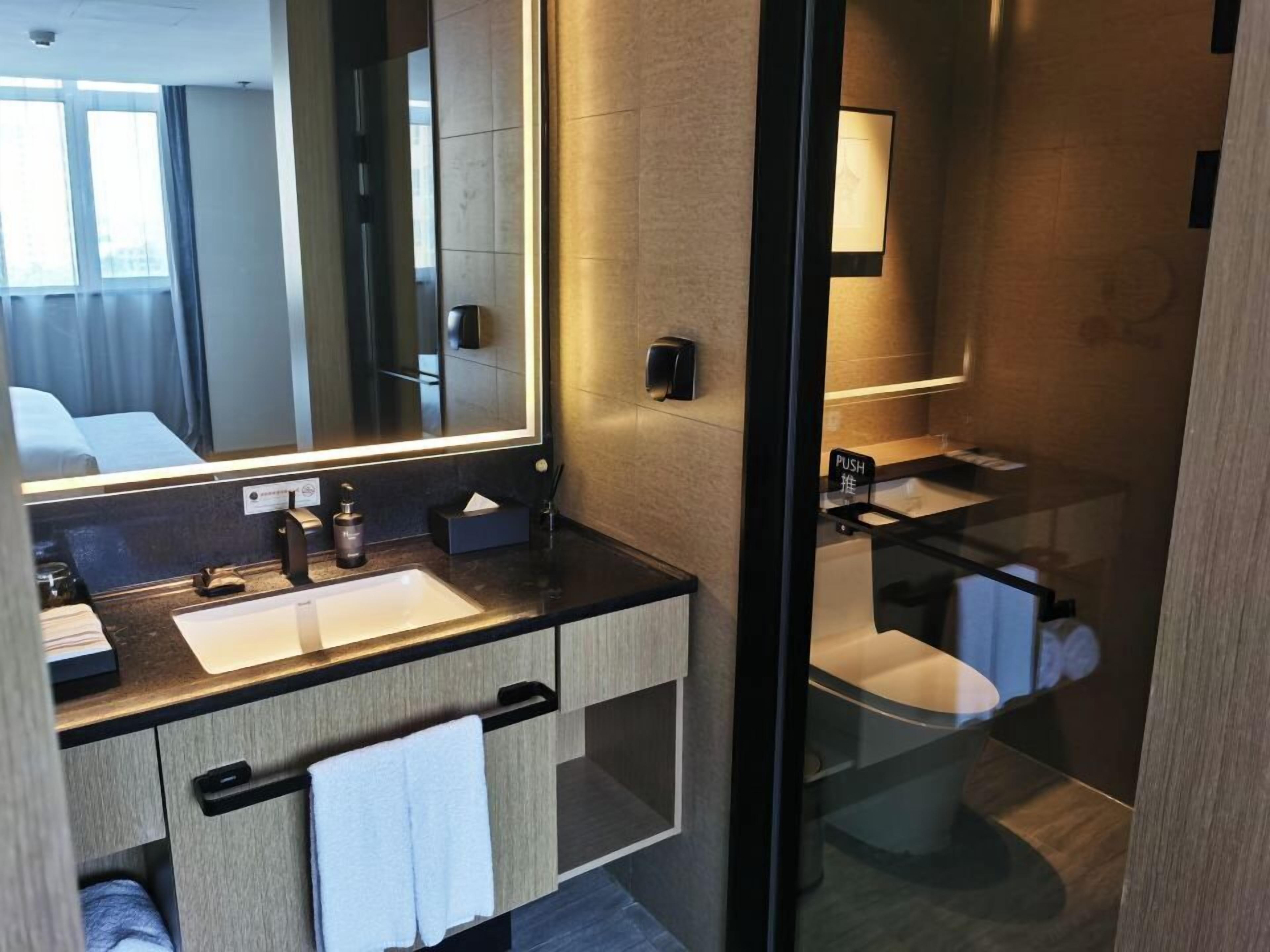 Ein modernes Badezimmer mit einem großen Spiegel, einem Waschbecken und einer Toilette.
