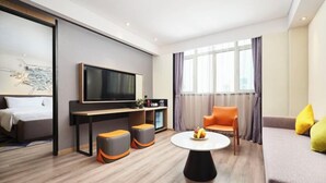 A modern hotel room with a bed, a TV, a sofa, a coffee table, and a dining table with fruit. - Wanda Moments Heze (Heze)