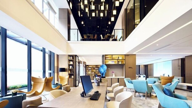 A modern, multi-level lounge area with a central table, comfortable seating, and a ceiling with geometric light fixtures. - Wanda Moments Heze (Heze)
