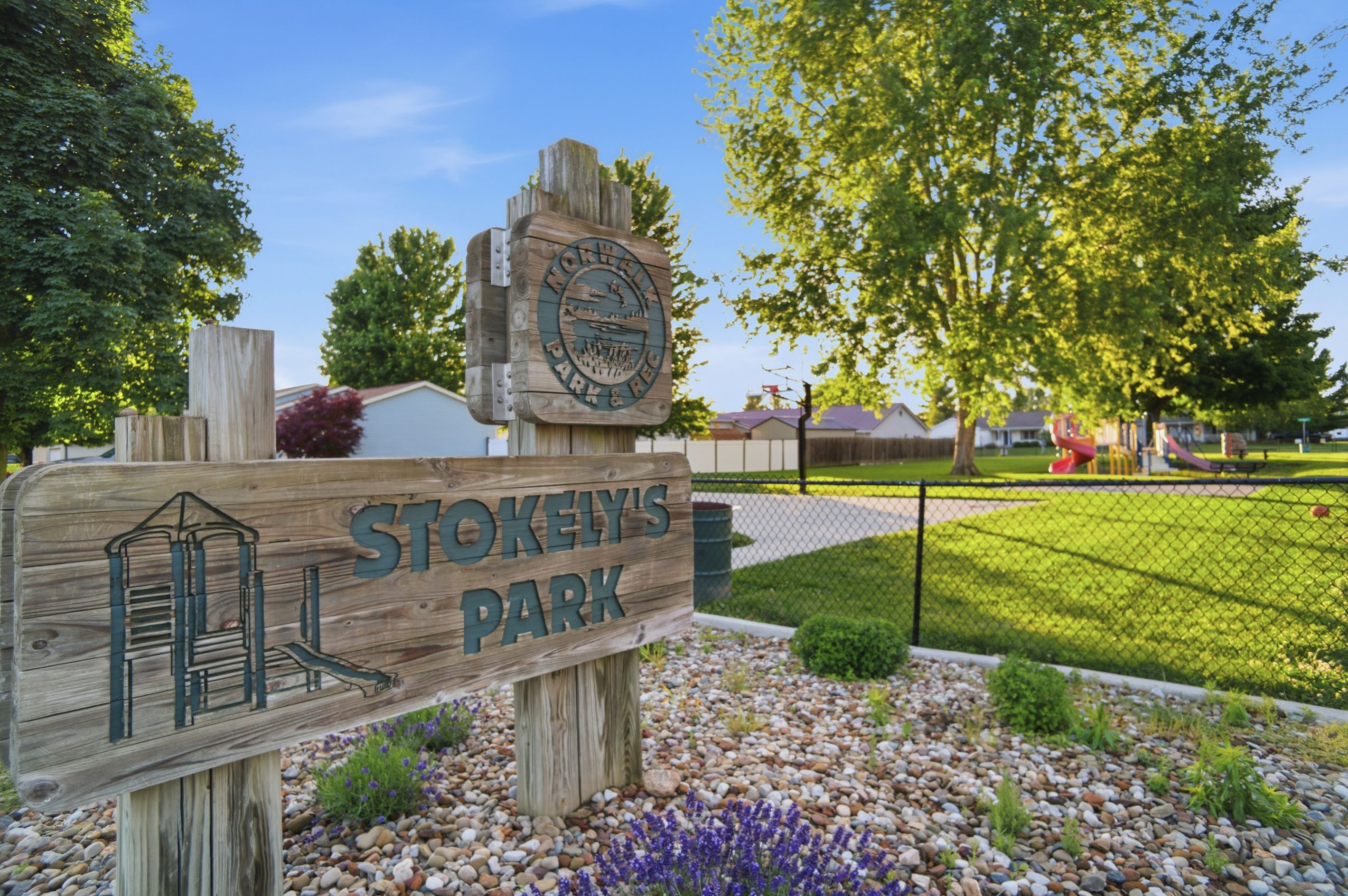 A wooden sign for Stokely's Park with a depiction of a building and a park scene.