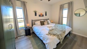 Une chambre à coucher comprenant un lit, un ventilateur de plafond, une table de chevet, un miroir et une fenêtre avec des rideaux.