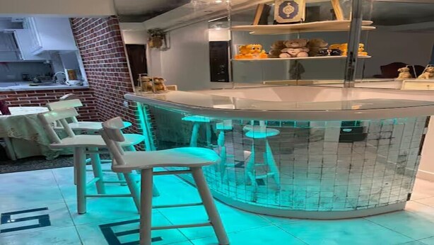 Een bar met krukken en een betegelde vloer, een keuken op de achtergrond en planken met knuffeldieren.