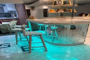 A bar area with stools and a tiled floor, a kitchen in the background, and shelves with stuffed animals. - Comfy Apartment (Cairo)