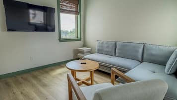 Ein Wohnzimmer mit einer Couch, einem Holztisch, einem an der Wand befestigten Fernseher und einem Fenster mit Jalousien.
