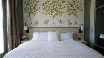 A hotel room with a large bed, two bedside lamps, a nightstand with a vase of flowers, and a wall mural of trees.
