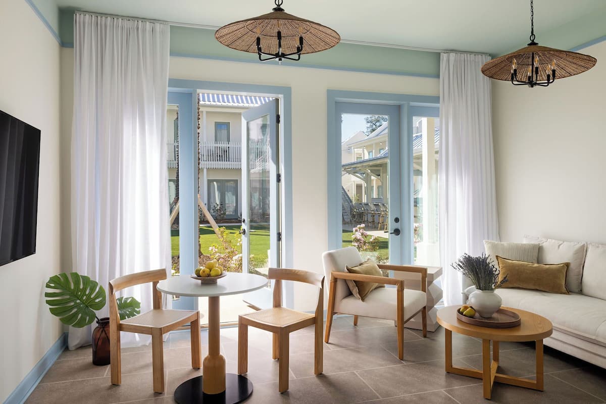 A room with a dining table, chairs, a sofa, a coffee table, and a hanging light fixture.
