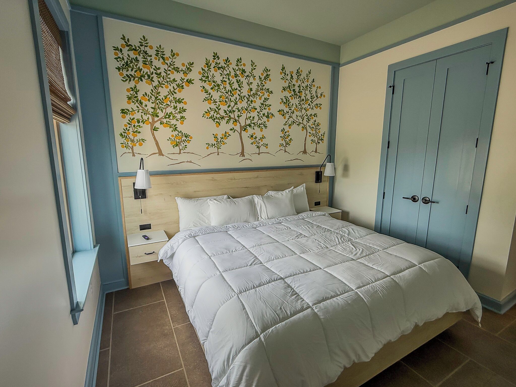 Un dormitorio con cama, mesita de noche, lámpara, estante en la pared y una puerta.